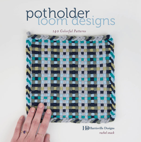 A hand rests on a woven square potholder made of blue, gray, black, and green bands, centered on the cover of a book titled potholder loom designs: 140 Colorful Patterns by Rachel Snack.
