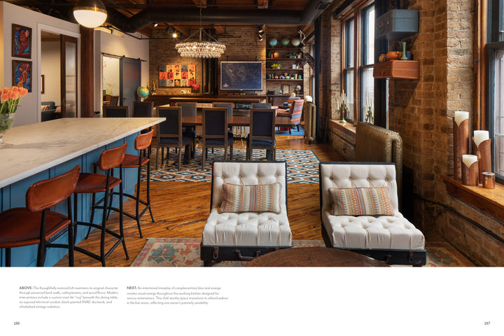 The "Midwest Home" by Schiffer Publishing, Ltd. showcases two tufted white lounge chairs, patterned pillows, a blue kitchen island with bar stools, exposed brick walls, large windows, unique art, and wood floors with decorative rugs.