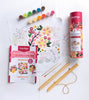 The ColorMaps Paint-by-Number Beautiful Blooms kit by Schiffer Publishing, Ltd. sits on a table with paint pots, two brushes, a vibrant floral outline sheet, folded instructions, and a pink cylindrical ColorMaps container.