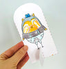 A hand holds a cut-out paper drawing from Pumpkin Patch Pals by Schiffer Publishing, Ltd., featuring an orange and yellow owl with a blue hat and suspenders against a white background—perfect for autumn-themed art projects or paper craft coloring books.