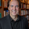 A man with medium-length brown hair and a playful Milk Mustache smiles at the camera in a warmly lit library, wearing a black suit—reminiscent of classic ads. Product: Milk Mustache by Schiffer Publishing, Ltd.