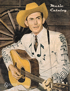 A man in a cowboy hat and a suit decorated with musical notes sits playing an acoustic guitar, with a wagon wheel and wooden wall in the background. The words Music Catalog appear in the upper right corner.