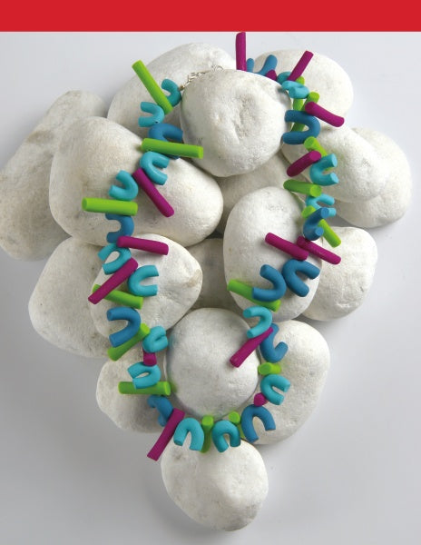 A Schiffer Publishing, Ltd. Costume Jewelry necklace with blue, green, and purple beads is displayed on smooth white stones, set against a white background with a red band at the top.